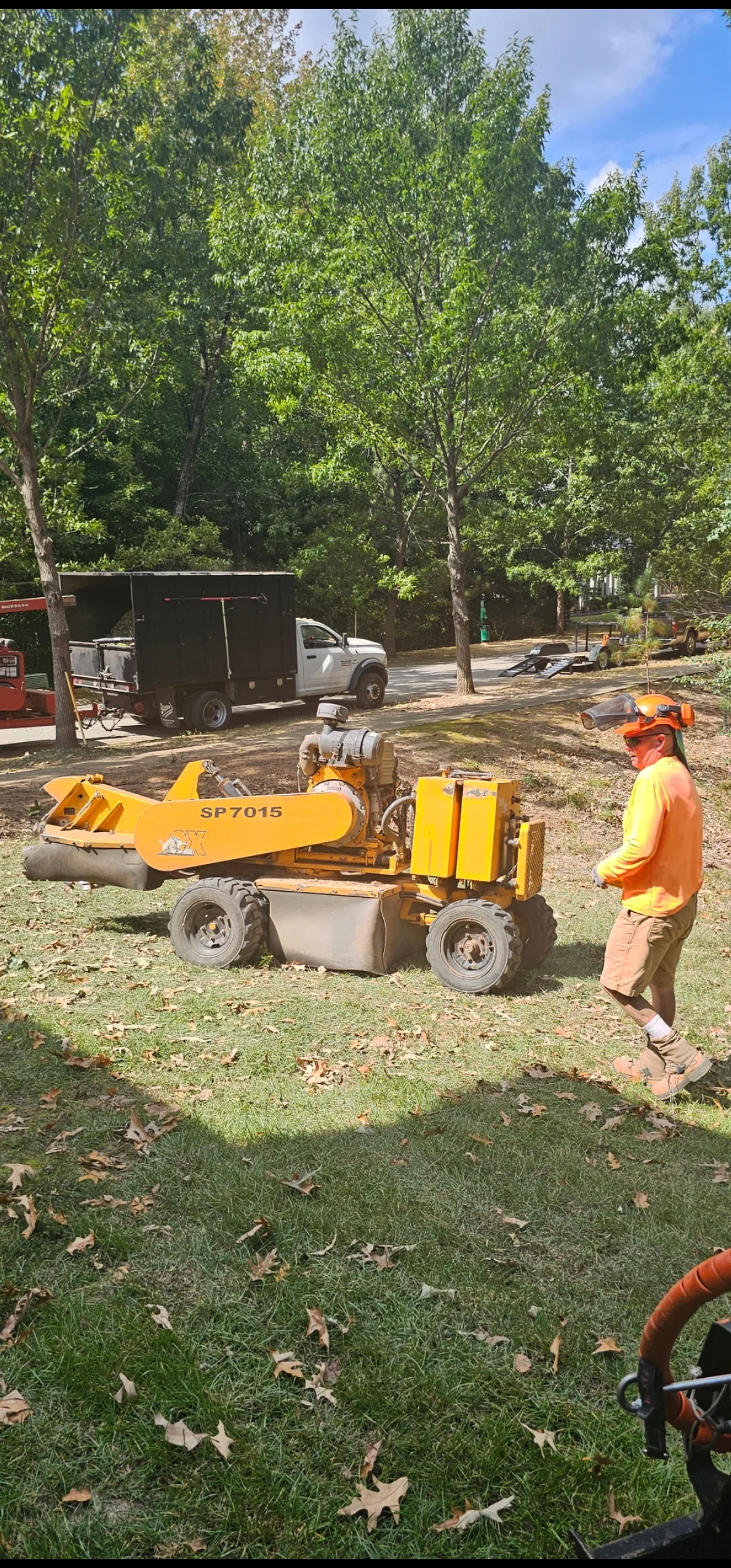 Tree service crew operating yellow wood chipper with processed debris in residential yard