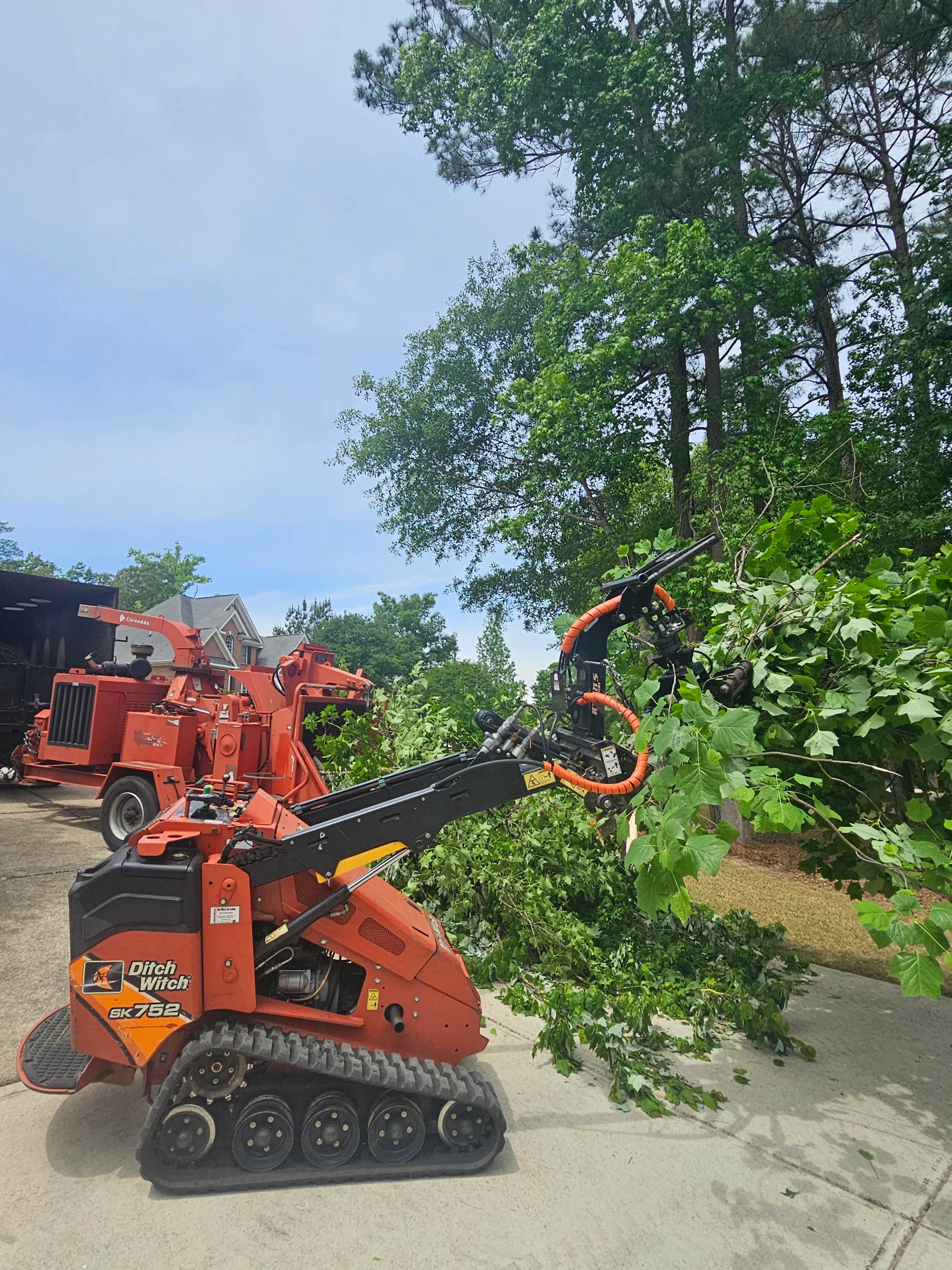 Red Ditch Witch wood chipper processing tree branches with service truck in background